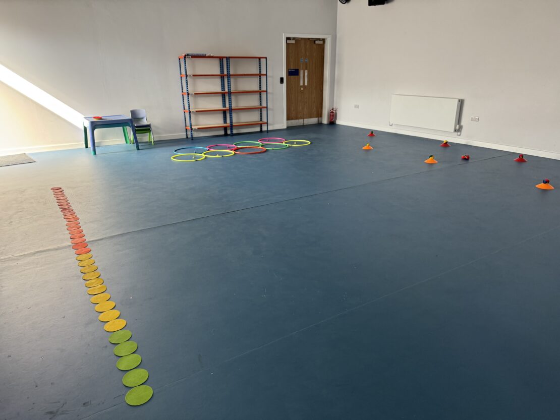 A large hall space with games equipment such as colourful cones and hoops set out on the floor.